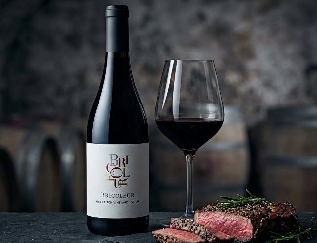 2022 Bricoleur Vineyards Kick Ranch Syrah bottle and wine glass paired with a pepper-crusted ribeye steak